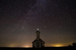 une petite chapelle avec une croix éclairée sur fond de ciel étoilé - Photo de Andrew Seaman sur https://unsplash.com/fr/photos/Y3WEhjQivTI 