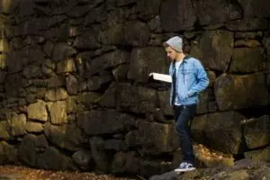 Un jeune homme march een lisant sa bible devant un mur fait de grosses pierres - Photo de Jeremy McKnight sur https://unsplash.com/fr/photos/GTriI3JMRMY