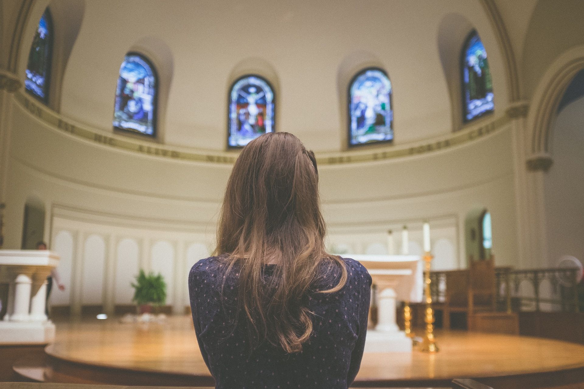 une femme seule, de dos, regardant le choeur d'une église, les vitraux, l'autel - Photo de Kenny Eliason sur https://unsplash.com/fr/photos/b7YCNt1vihM