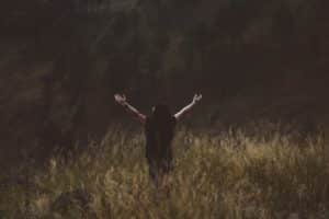 Une femme, de dos, lève les bras en priant dans un pré aux hautes herbes - Photo de Hanny Naibaho sur https://unsplash.com/fr/photos/djLvhqqzesU