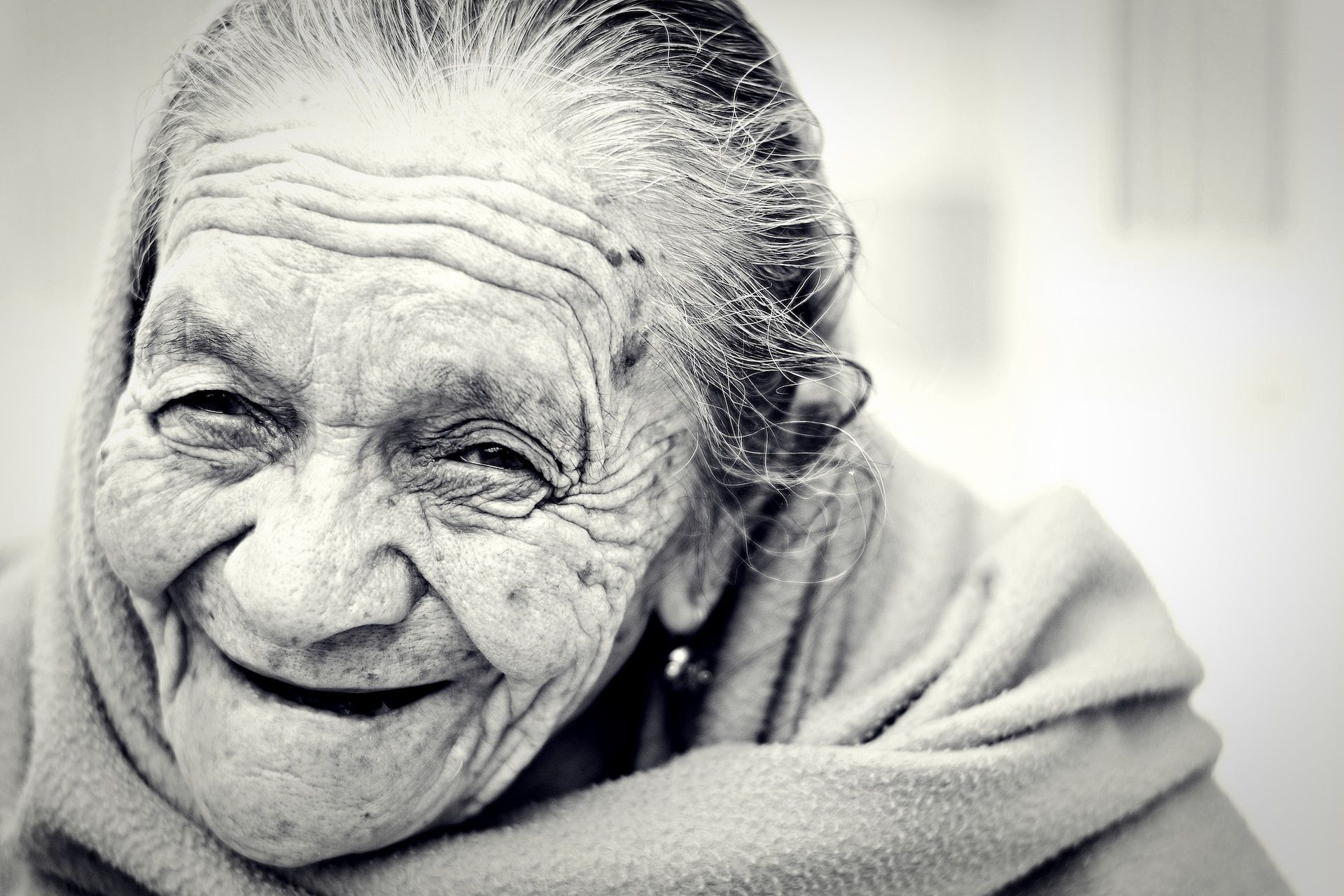Photo en noir et blanc du visage d'une femme très âgée et souriante - Photo de Danie Franco sur https://unsplash.com/fr/photos/o1PKM7-8AH4