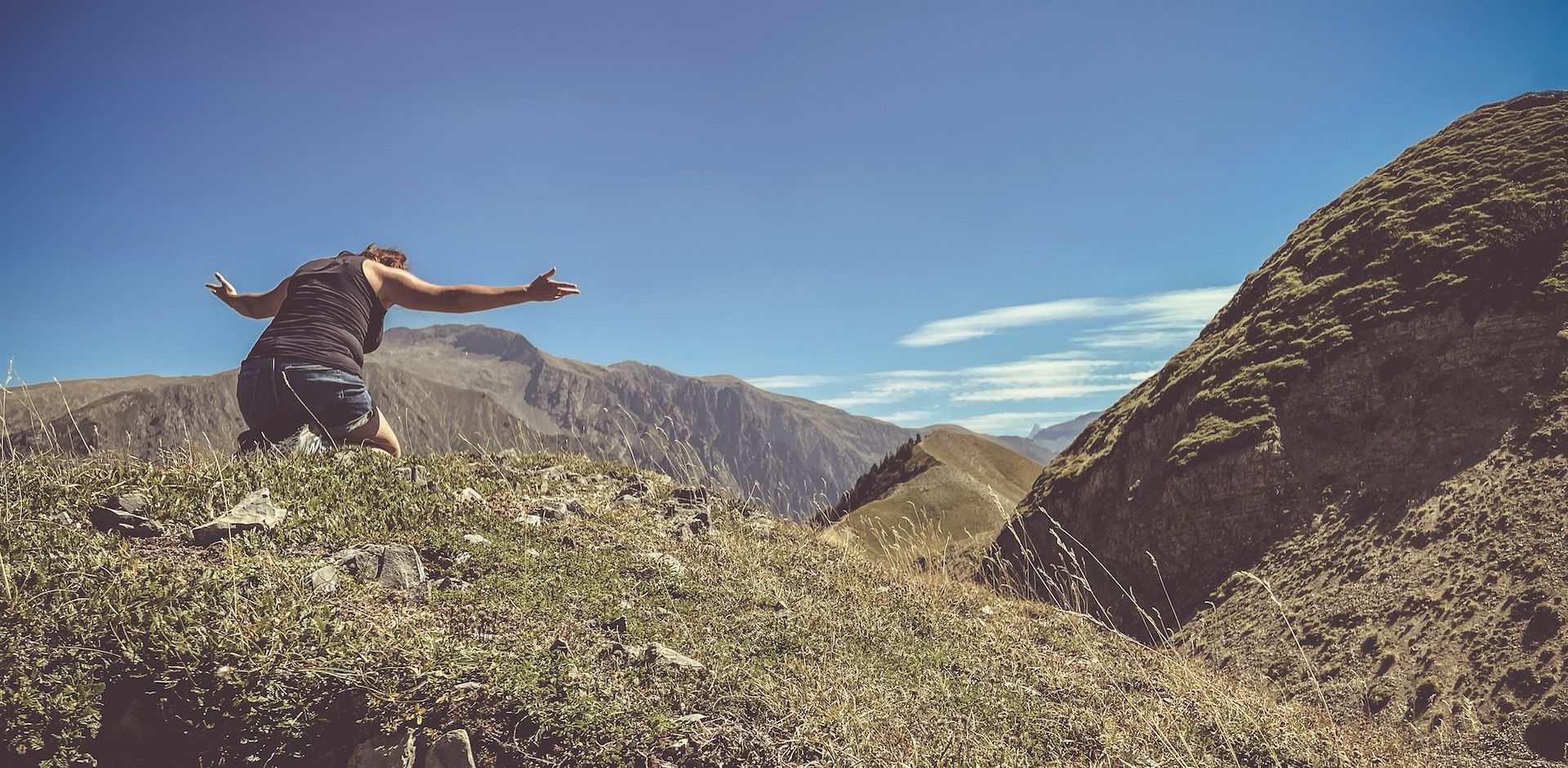 En montagne, une femme à genoux, élevant les bras vers Dieu - Photo de Jametlene Reskp sur https://unsplash.com/fr/photos/un-homme-debout-au-sommet-dune-colline-verdoyante-BjxB-TZa2RM