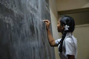 Une jeune fille en uniforme scolaire écrit au tableau - Photo de Nikhita S sur https://unsplash.com/fr/photos/NsPDiPFTp4c