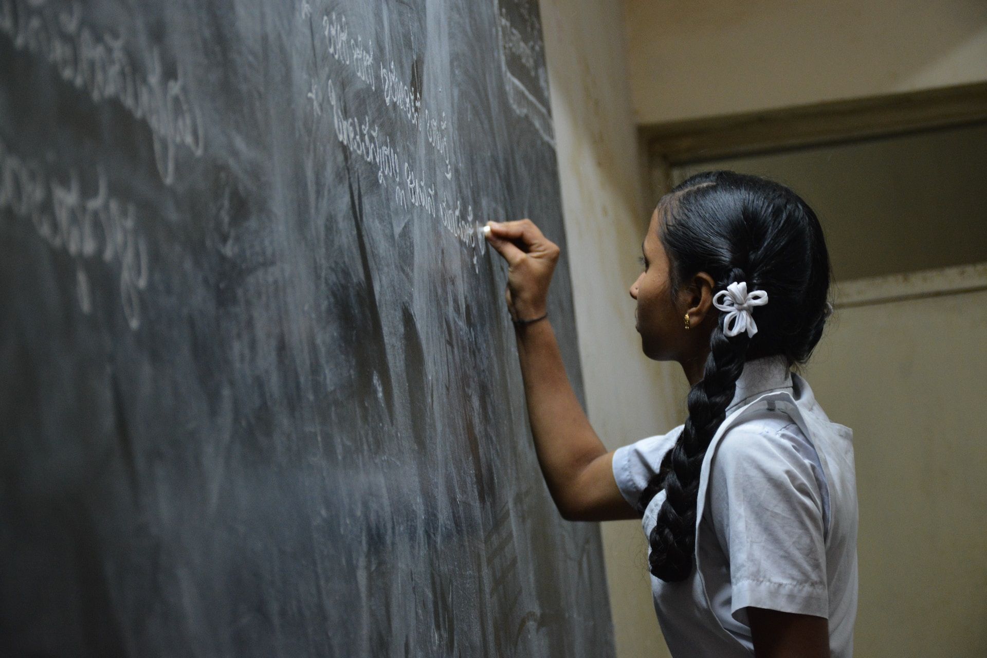 Une jeune fille en uniforme scolaire Ã©crit au tableau - Photo de Nikhita S sur https://unsplash.com/fr/photos/NsPDiPFTp4c