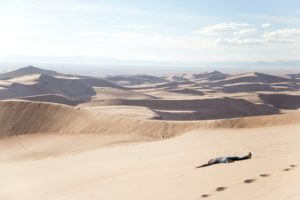 Paysage de désert avec un homme allongé dans le sable, les bras en croix - Photo de Vlad Tchompalov sur https://unsplash.com/fr/photos/homme-couche-sur-le-desert-pendant-la-journee-EeiOu_OyuSY