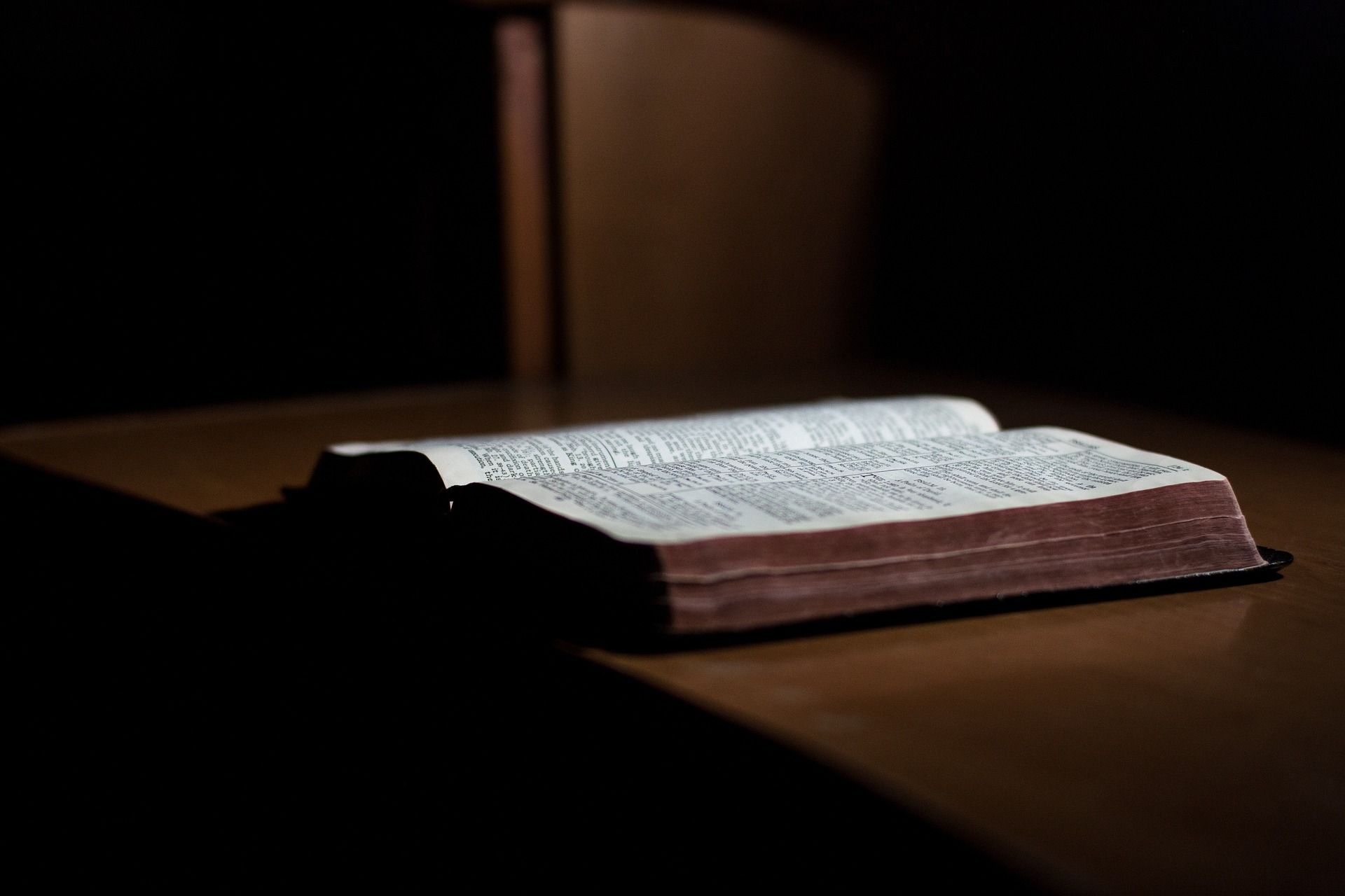 Une bible posée sur une table en bois avec un fond sombre - Image par StockSnap de https://pixabay.com/fr/photos/livre-bible-en-train-de-lire-table-2596785/