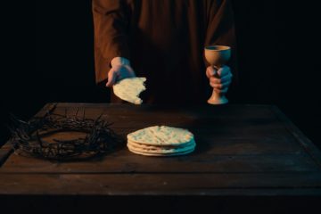 Photo représentant le Christ tendant le pain rompu et la coupe de vin, avec posée sur la table sa future couronne d'épine - Photo de Rey Proenza sur https://unsplash.com/fr/photos/une-personne-tenant-un-verre-a-vin-et-un-verre-a-vin-O98dk75B_t4