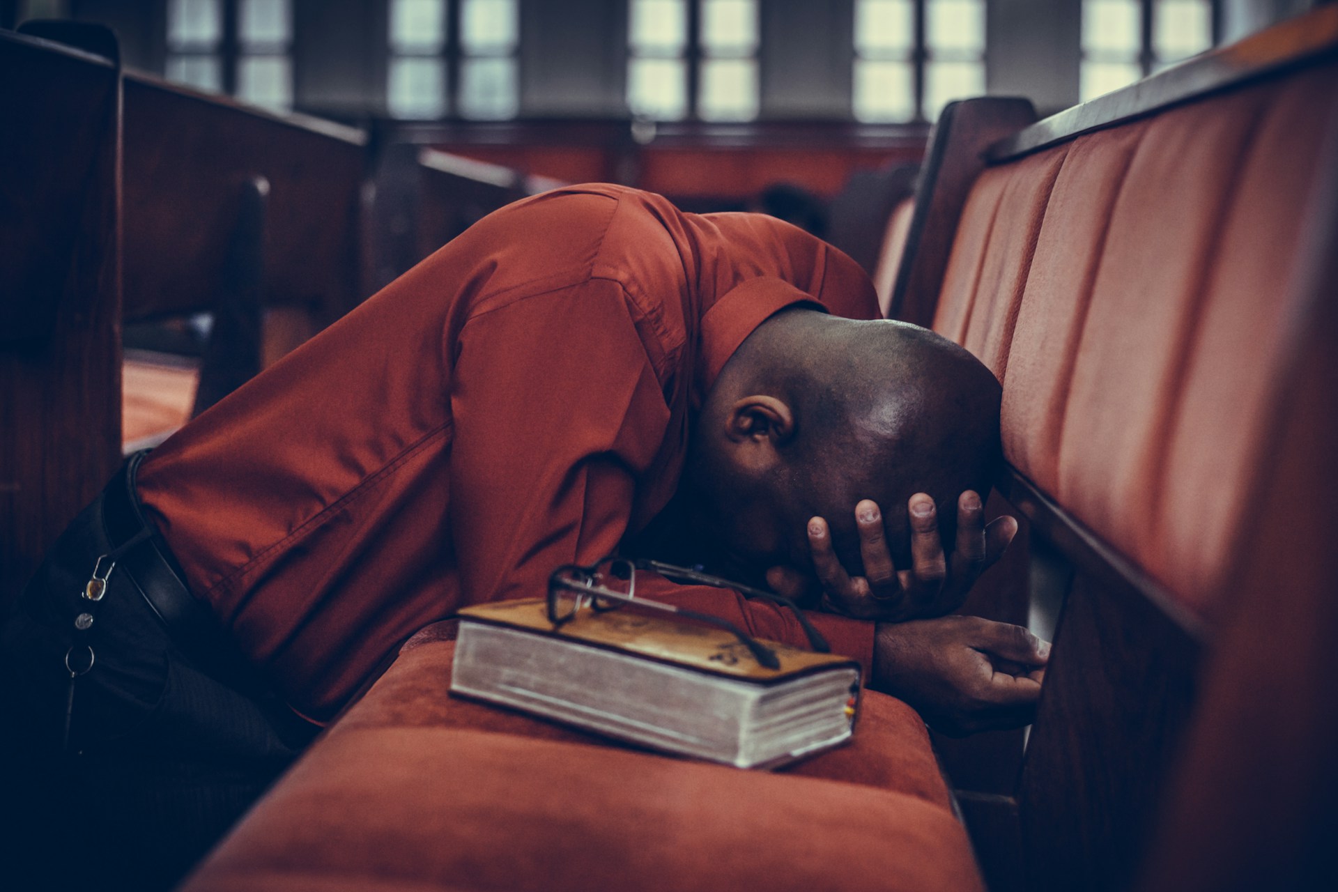Un homme en prière dans une église, avec sa Bible posée à côté d elui - Photo de Samuel Martins sur https://unsplash.com/fr/photos/homme-en-haut-orange-a-cote-de-lunettes-sur-un-livre-brun-3U7HcqkIbb4