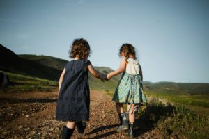 Une petite fille en aide une autre à marcher dans l'herbe - Photo de Josue Michel sur https://unsplash.com/fr/photos/2-girls-in-blue-dress-standing-on-brown-field-during-daytime-xCU7nCMNfI8