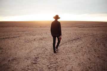 Un homme en noir avec un chapeau et une Bible en main marche dans un pré desséché - Image par StockSnap de https://pixabay.com/fr/photos/homme-mec-chapeau-gazon-s%C3%A9ch%C3%A9-2589900/