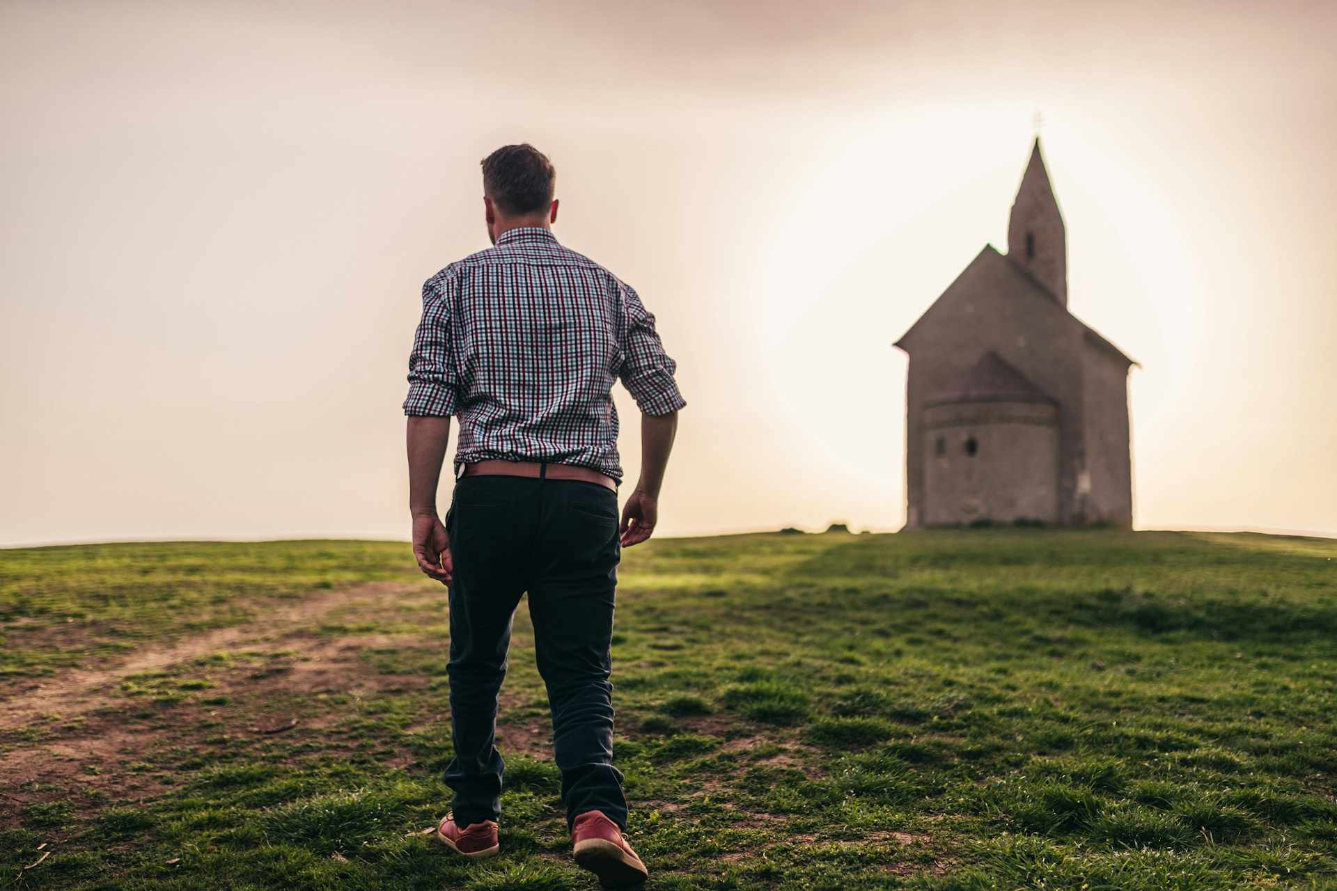 Un homme marche dans la nature en se détournant d'une église qui est en arrière plan - Photo de Peter Dlhy sur https://unsplash.com/fr/photos/homme-marchant-dans-lherbe-verte-Ty9uAw5Tl3g