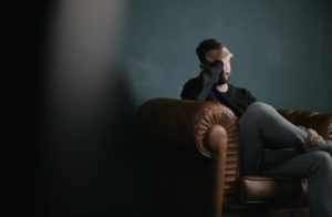 Un homme barbu assis sur le fauteuil se prend le visage avec sa main, l'air inquiet - Photo de Nik Shuliahin 💛💙 sur https://unsplash.com/fr/photos/un-homme-se-tient-la-tete-alors-quil-est-assis-sur-un-canape-BuNWp1bL0nc