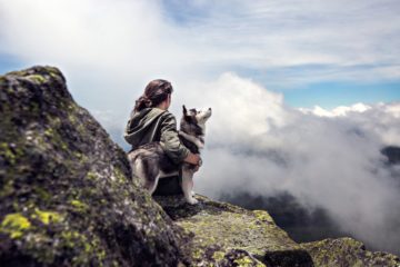 une femme avec son chien assis en montagne regardant le ciel et les nuages - Image par Pexels de https://pixabay.com/fr/photos/ciel-femme-des-nuages-fille-1283446/