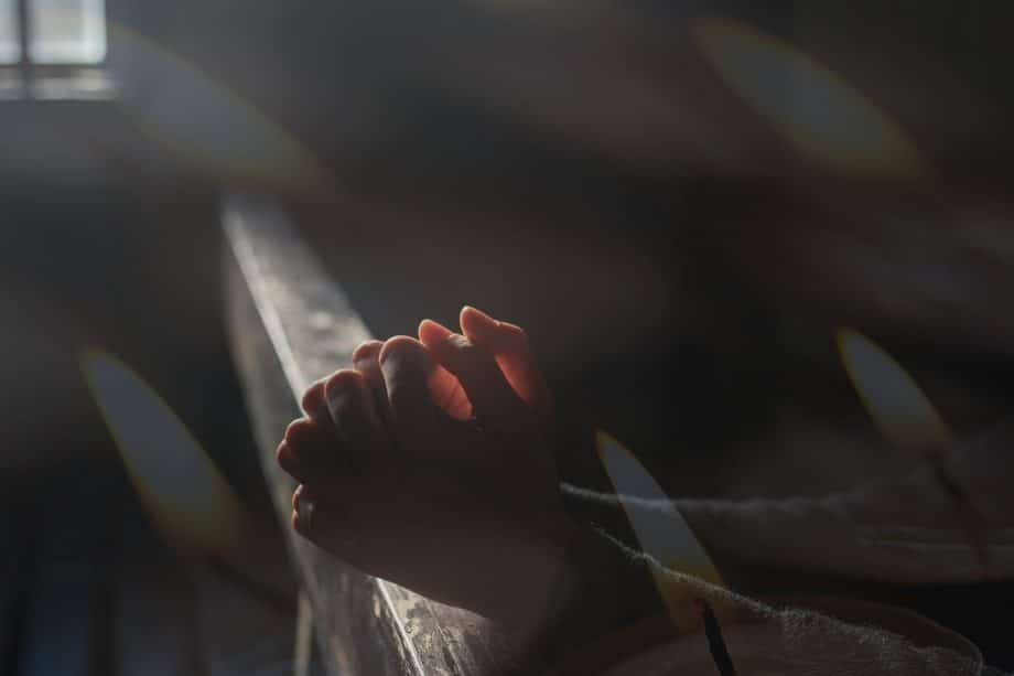 deux mains croisées en prière, dans une église sombre, éclairée par une petite fenêtre - Image par Ri Butov de https://pixabay.com/fr/photos/pri%C3%A8re-foi-religion-esp%C3%A9rer-6764197/