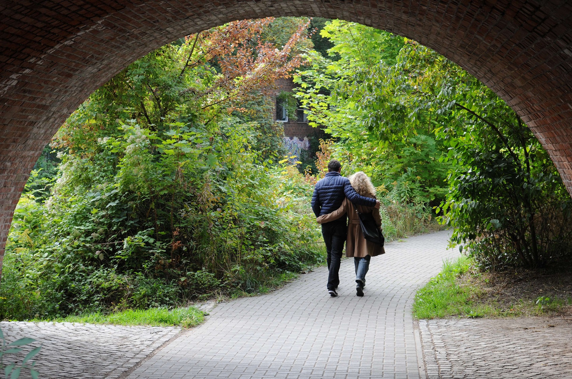 Un couple marche en se tenant par la taille sur une route qui passe sous un pont et va dans la nature - Image par Rainer Küster de https://pixabay.com/fr/photos/pont-peu-paire-homme-femme-525615/