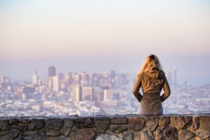Une jeune femme blonde, vue de dos, assise sur un muret, regarde un panorama sur la ville - Image par Pexels de https://pixabay.com/fr/photos/blonde-s%C3%A9ance-mur-immeubles-ville-1867768/