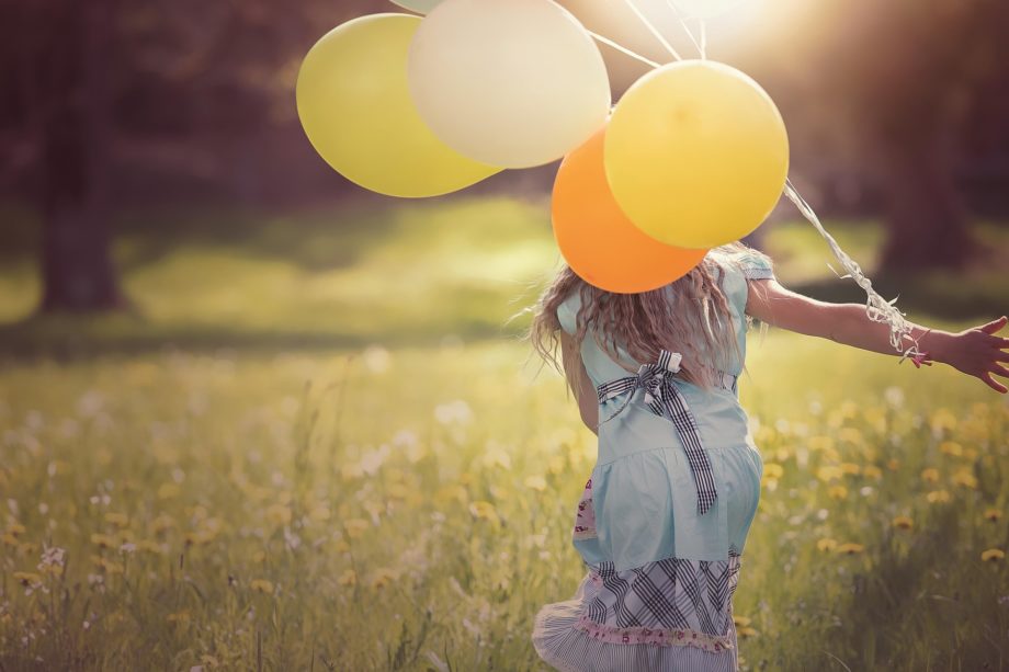 Une fille court dans un pré en traînant des ballons multicolores - Image par Petra de https://pixabay.com/fr/photos/fille-des-ballons-enfant-content-1357485/