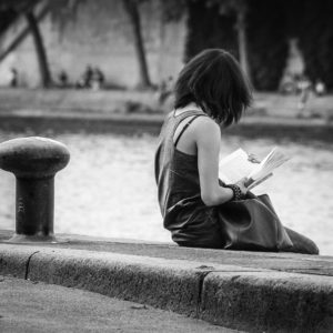 Photo en noir et blanc d'une jeune femme lisant un livre assise sur le bord d'un canal. Image par Patrick Marty de https://pixabay.com/fr/photos/fille-seine-paris-lecture-livre-803812/