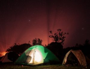 Trois tentes de camping sous un ciel étoilé, celle du milieu est illuminée de l'intérieur - Photo de Tadeu Jnr sur https://unsplash.com/fr/photos/tente-exterieure-eclairee-en-vert-XdIOaD30OEU