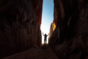 Un homme marche dans un étroit canyon et lève les bras au ciel en arrivant au bout - Image by John Paul Edge from https://pixabay.com/photos/canyon-gorge-silhouette-man-rocks-4641080/