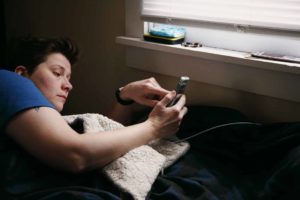 Une jeune femme dans son lit regarde son téléphone avec inquiétude - Photo de Shane sur https://unsplash.com/fr/photos/homme-en-chemise-noire-tenant-un-smartphone-noir-35bnMbid2rQ