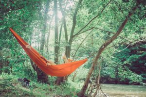 Une femme presque entièrement cachée dans un hamac orange, dans une forêt luxuriante - Image par StockSnap de https://pixabay.com/fr/photos/gens-femme-hamac-nature-fleuve-2587988/
