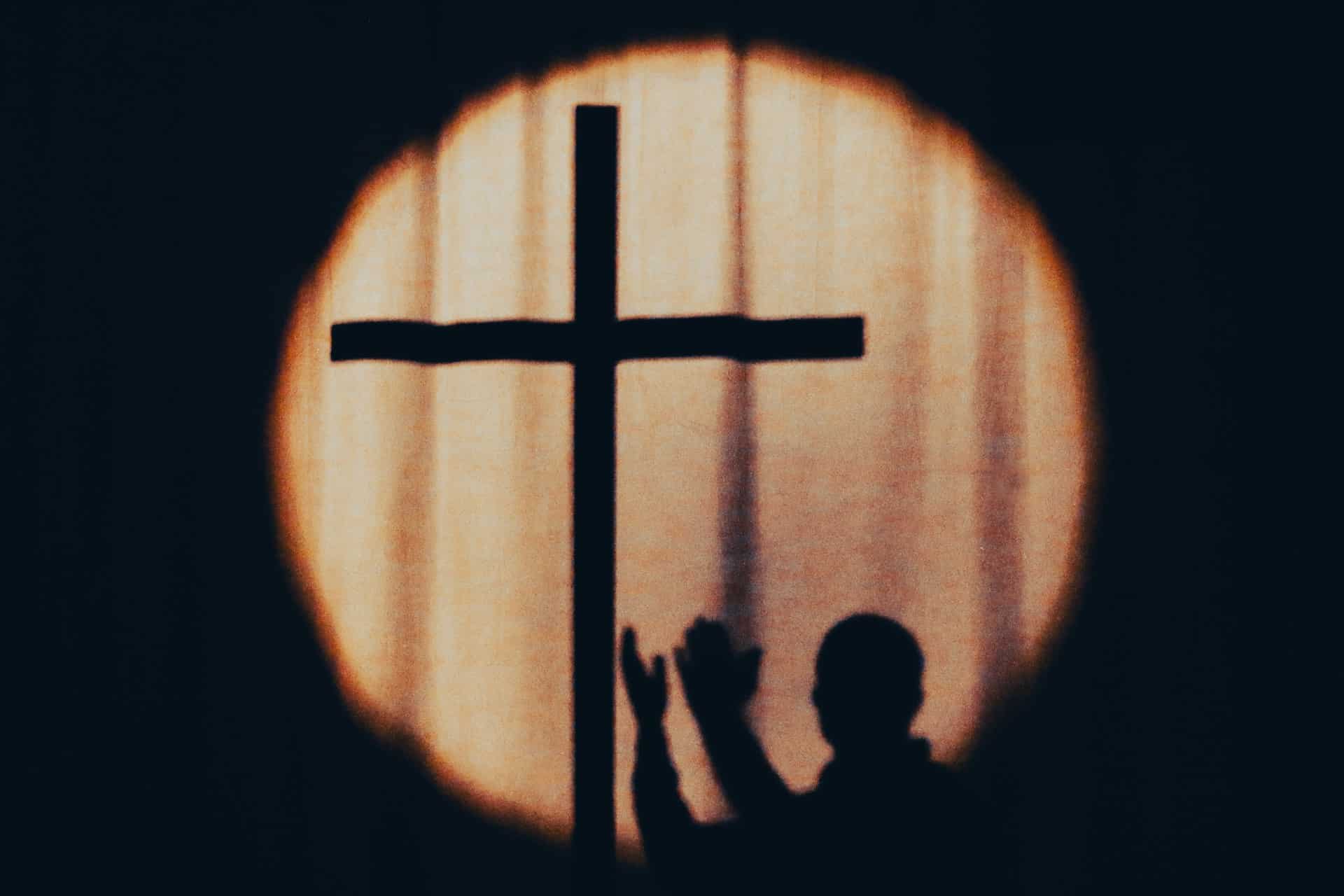 En ombre chinoise : un homme tend les bras vers la croix - Photo de Jametlene Reskp sur https://unsplash.com/fr/photos/silhouette-dune-personne-tenant-une-croix-devant-une-fenetre-7Rs8wr87R_U