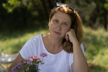 Une femme dans la quarantaine, tranquille, posant avec un bouquet de leurs dans la nature, regarde l