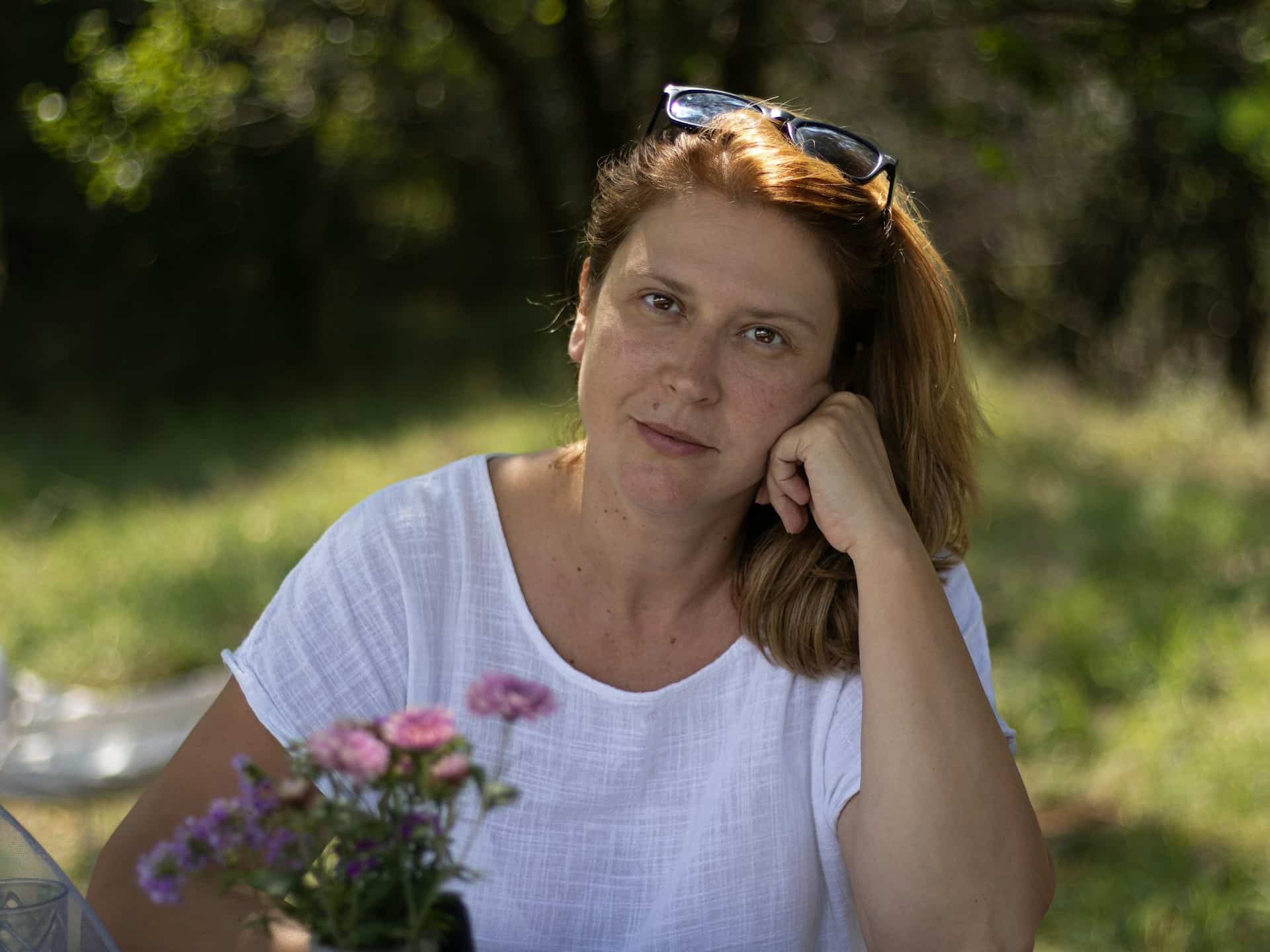 Une femme dans la quarantaine, tranquille, posant avec un bouquet de leurs dans la nature, regarde l'objectif - Photo de Anita Jankovic sur https://unsplash.com/fr/photos/une-femme-assise-a-une-table-avec-un-vase-de-fleurs-EQCZovcgz9A