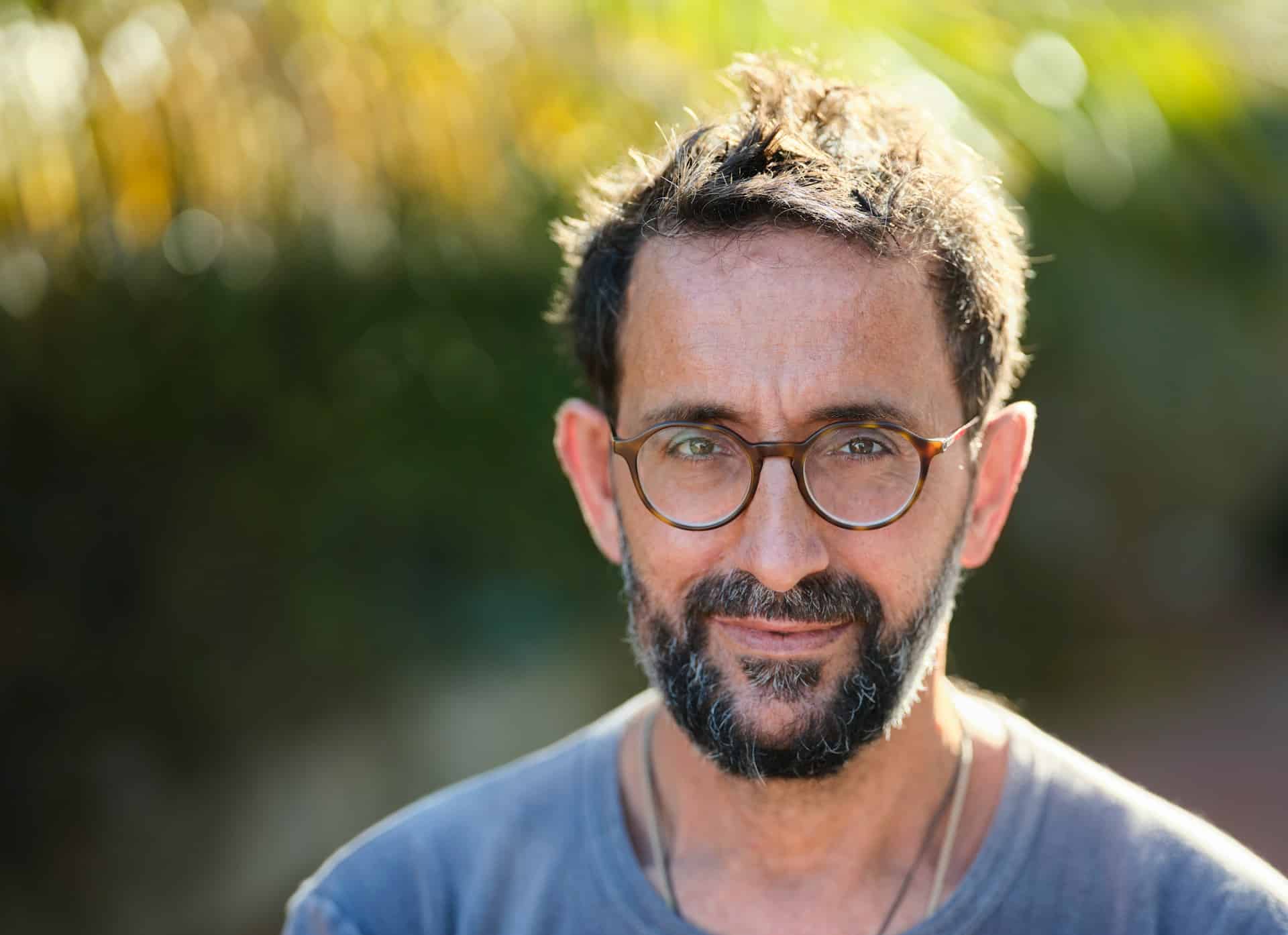 Un homme d'une cinquantaine d'années souriant sur fond de nature - Photo de Christian Buehner sur https://unsplash.com/fr/photos/homme-en-chemise-bleue-a-col-rond-portant-des-lunettes-a-monture-noire-zYD6ou1Qj10