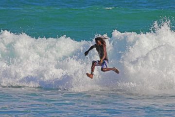 Un jeune surfeur aux cheveux longs semble marcher sur l