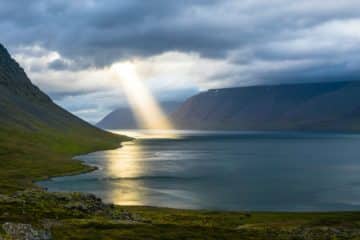 Un rayon de soleil passe à travers des nuages et éclairent un bras de mer - Photo de Davide Cantelli sur https://unsplash.com/fr/photos/reflet-du-soleil-sur-leau-calme-pres-des-montagnes-vertes-H3giJcTw__w