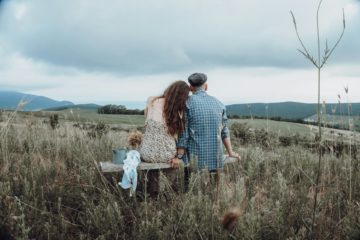 Face à la nature, un banc où sont assis une femme et un homme, avec une place sans personne à coté d