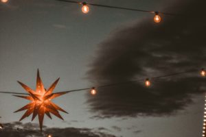 Une étoile en papier, illuminée de l'intérieur, sur fond de nuages sombres, symbolisant la lumière de la fête chrétienne - Photo de Ryan sur https://unsplash.com/fr/photos/un-objet-en-forme-detoile-sur-un-fil-fKV3K1bRkh4
