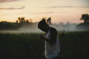 Un jeune homme dans la nature, au coucher du soleil, en pleine réflexion ou prière - Photo de Jake Young sur https://unsplash.com/fr/photos/homme-portant-un-haut-raglan-noir-et-blanc-sur-un-champ-dherbe-verte-IsCT80pMA8k