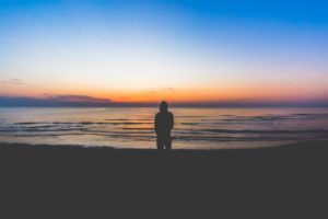 Une personne regarde la nuit qui vient face une mer calme - Photo de Pietro De Grandi sur https://unsplash.com/fr/photos/silhouette-de-personne-debout-pres-de-la-mer-pendant-lheure-dor-KF3GJ3DYhY8