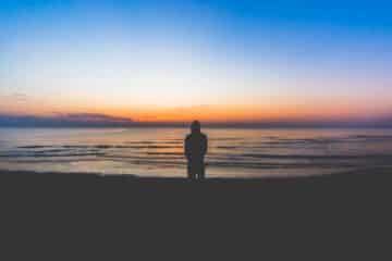 Une personne regarde la nuit qui vient face une mer calme - Photo de Pietro De Grandi sur https://unsplash.com/fr/photos/silhouette-de-personne-debout-pres-de-la-mer-pendant-lheure-dor-KF3GJ3DYhY8