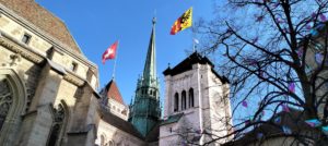 La cathédrale Saint-Pierre, avec les drapeaux de la Suisse et du canton de Genève pavoisant les tours - Photo de Roshand Bhantooa sur https://unsplash.com/fr/photos/une-eglise-avec-un-clocher-et-une-tour-dhorloge-IJJSz4Wvlhw