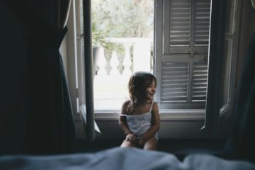Une fillette souriante et maquillée en chat est assise devant une fenêtre à moitié ouverte sur le jour qui se lève - Photo de Caroline Hernandez sur https://unsplash.com/fr/photos/fille-assise-pres-de-la-fenetre-pendant-la-journee-r1xJuG7rD60