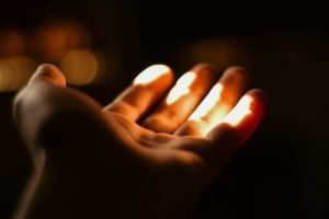 Une main ouverte comme pour recevoir, s'avance dans l'obscurité pour recevoir la lumière - Photo de NADER AYMAN sur https://unsplash.com/fr/photos/une-personne-tenant-une-bougie-allumee-dans-sa-main-1KH5oUafd2M