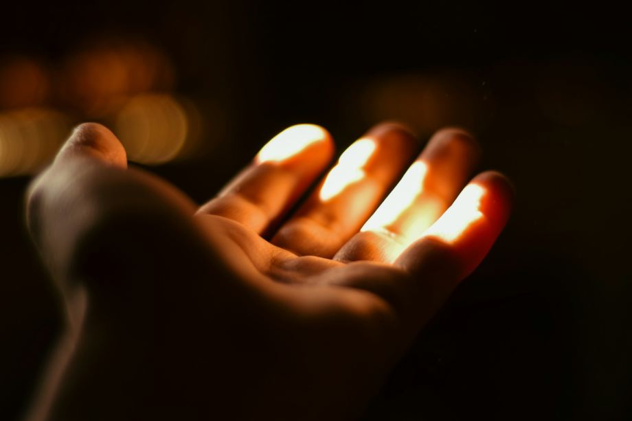 Une main ouverte comme pour recevoir, s'avance dans l'obscurité pour recevoir la lumière - Photo de NADER AYMAN sur https://unsplash.com/fr/photos/une-personne-tenant-une-bougie-allumee-dans-sa-main-1KH5oUafd2M