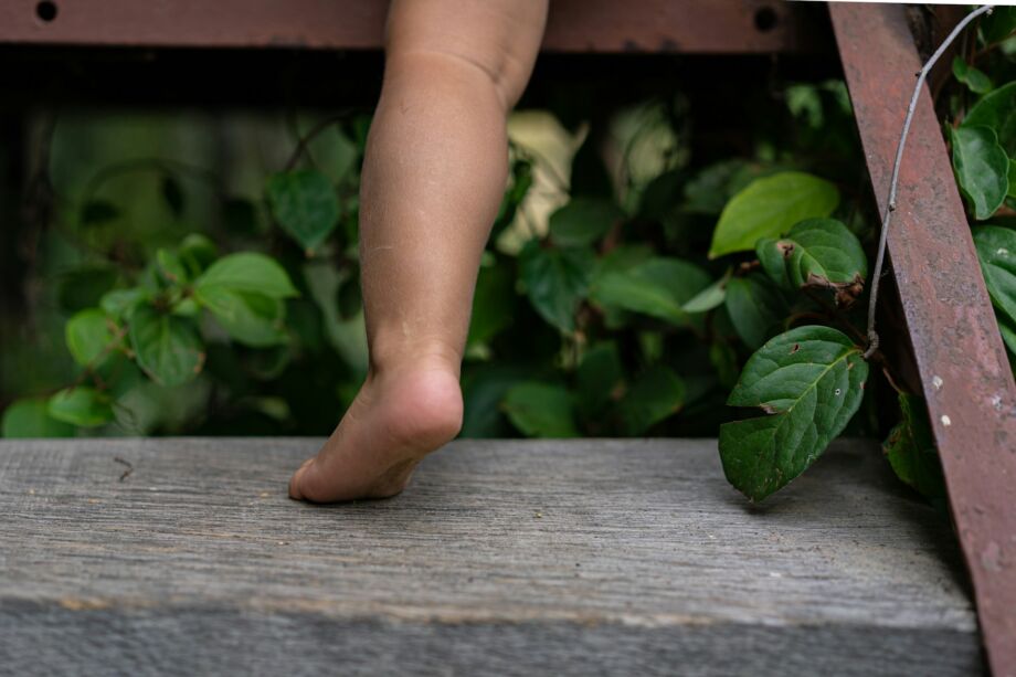 La petite jampe potelée d'un petit enfant sur des marches en bois brut - Photo de Anastasiia Krutota sur https://unsplash.com/fr/photos/pieds-de-personnes-sur-plancher-en-bois-brun-YpRqIwOV6KU