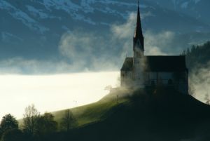Une belle église sur une crête surplombant un lac, en contre jour, dans la brume - Photo de Florian Haun sur https://unsplash.com/fr/photos/maison-noire-et-blanche-au-sommet-de-la-colline-otP-aR6zVgw