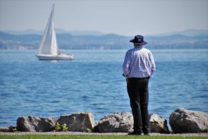 Unb homme de dos, au bord d'un lac, regarde un bateau à voile qui passe - Image by Julita from https://pixabay.com/photos/old-man-harbor-lake-constance-lake-4466290/