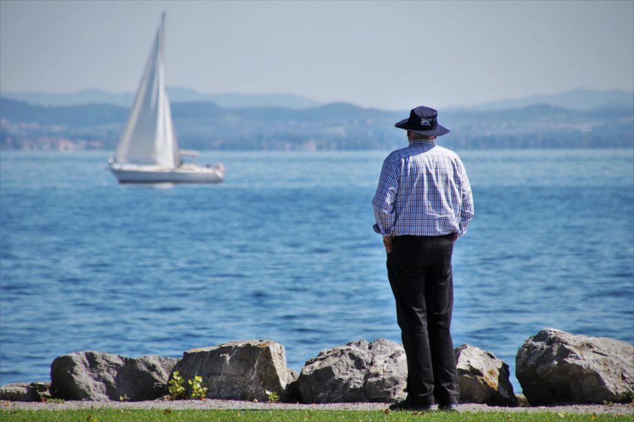 Unb homme de dos, au bord d'un lac, regarde un bateau à voile qui passe - Image by Julita from https://pixabay.com/photos/old-man-harbor-lake-constance-lake-4466290/