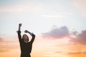 femme danse dans le soleil levant - Photo de Ludovica Dri sur https://unsplash.com/fr/photos/femme-en-chemise-noire-a-manches-longues-levant-la-main-droite-LsK74XvlDGM