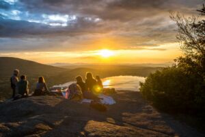 Des amis plus ou moins ensemble pour regarder un coucher de soleil sur la montagne et un lac - Photo de Arthur Poulin sur https://unsplash.com/fr/photos/group-of-people-sirring-under-sunset-NhU0nUR7920