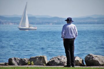 Un homme sur le bord du lac regarde un bateau à voile qui passe - Image par Julita de https://pixabay.com/fr/photos/vieil-homme-port-lac-de-constance-4466290/
