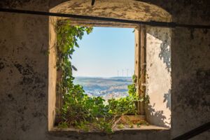 Vue sur un paysage de campagne avec des éoliennes, à travers la petite fenêtre d'une ruine envahie de lierre - Image par pstiegele de https://pixabay.com/fr/photos/la-fen%c3%aatre-lierre-envahi-mur-1817669/