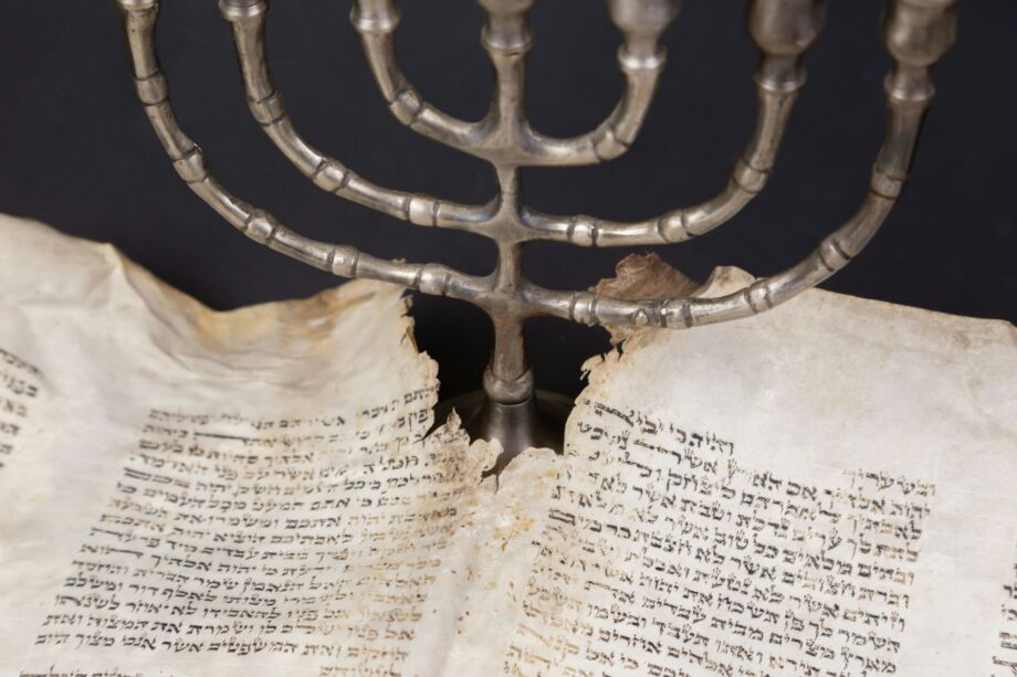 Un rouleau de la Torah usé est comme traversé par la lumière d'une Ménorah - Photo de Diana Polekhina sur https://unsplash.com/fr/photos/texte-7a79GN3AZMM